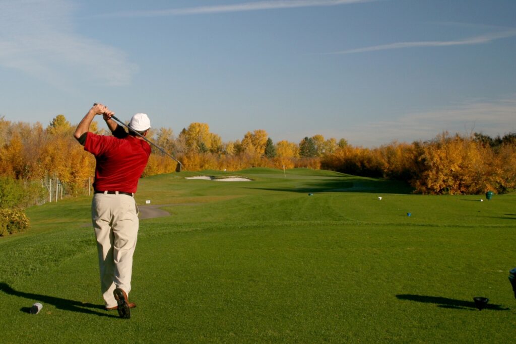 A man swinging a golf club in fall attire.