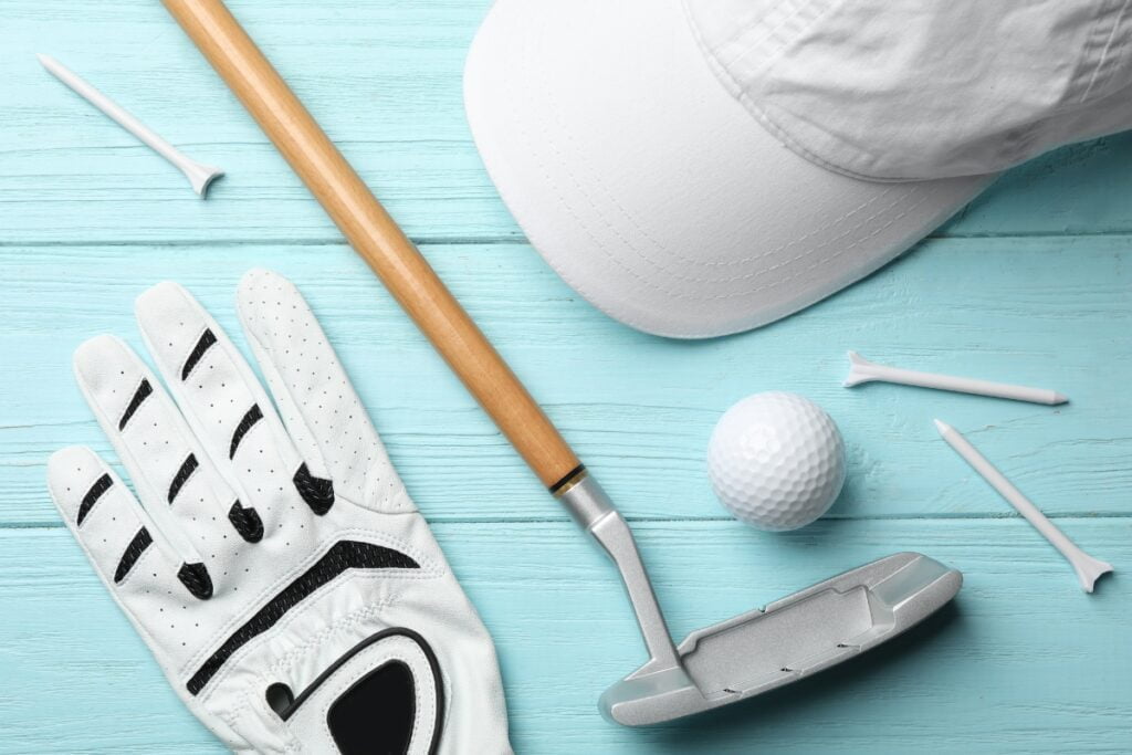 A golf club, hat, glove and putter on a blue wooden background featuring fall golf attire.