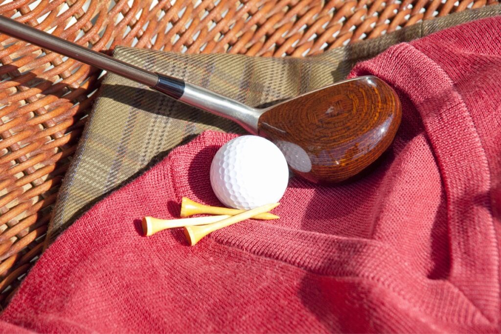 A golf club and a golf ball on a wicker basket, featuring fall golf attire.