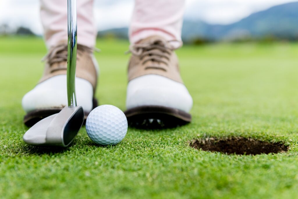 A golfer's feet next to a golf ball on a golf course while wearing compression golf socks.