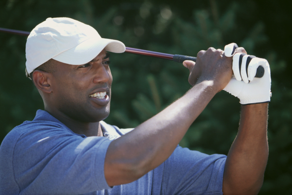 A man wearing a hat, swinging a golf club.