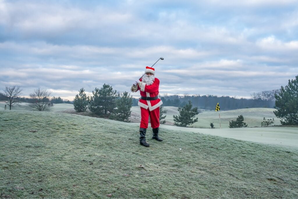 Santa Claus enjoying a round of golf on a winter course.