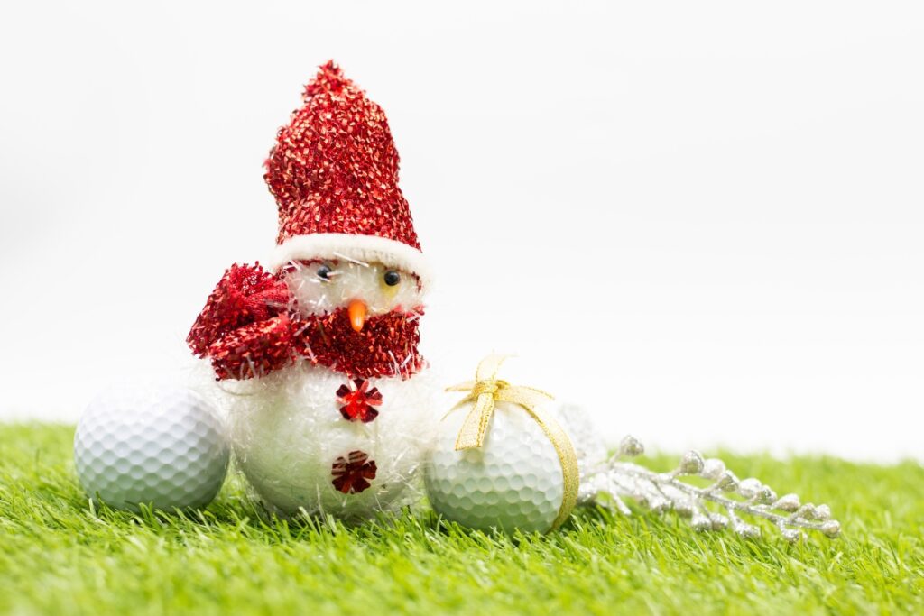 A golf ball and a snowman playing golf on the grass in the winter.