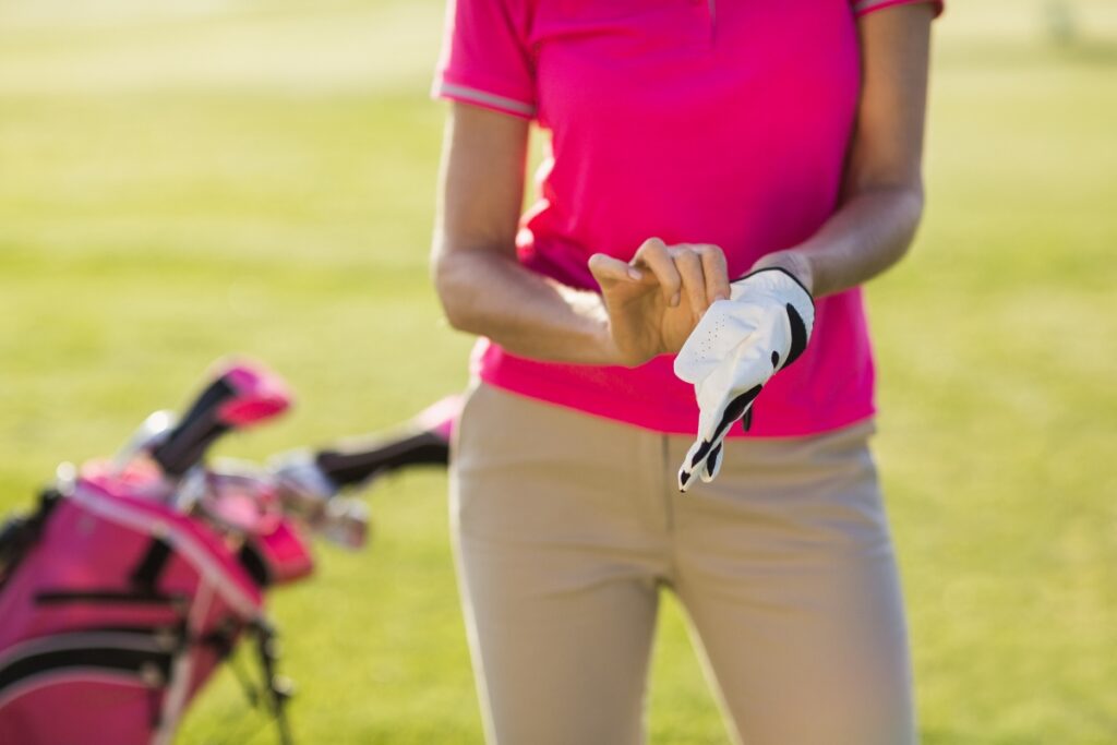 A woman is elegantly holding a golf club in her hand, wearing stylish casual golf wear.