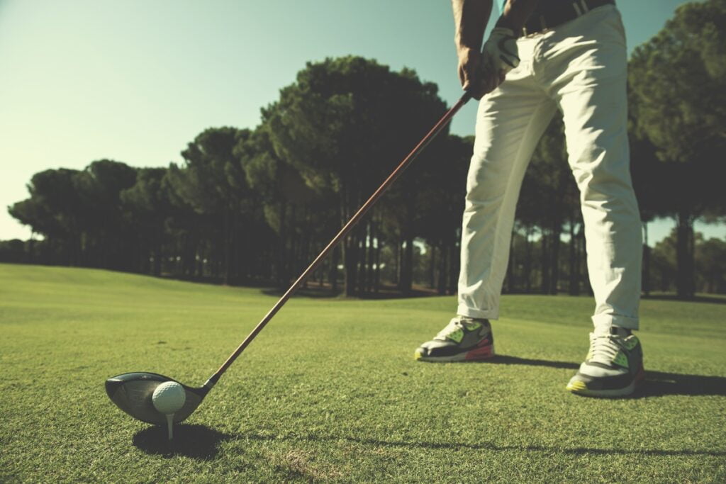 A man is standing on a golf course in casual golf wear with a golf club in his hand.