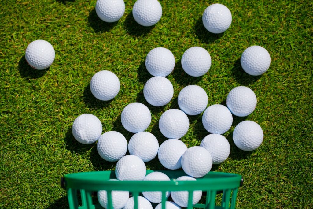 Modern white golf balls in a green basket on the grass.