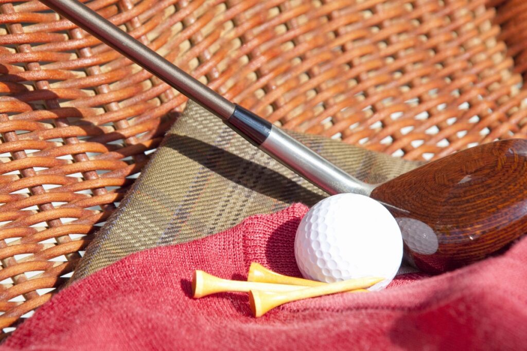 A pro golf apparel, a golf club, and a golf ball on a wicker basket.