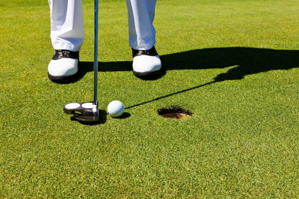 A man in pro golf apparel is putting a golf ball into a hole.