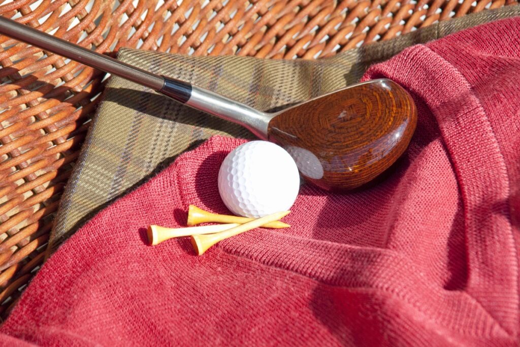 A pro golf apparel, a golf club, and a golf ball on a wicker basket.