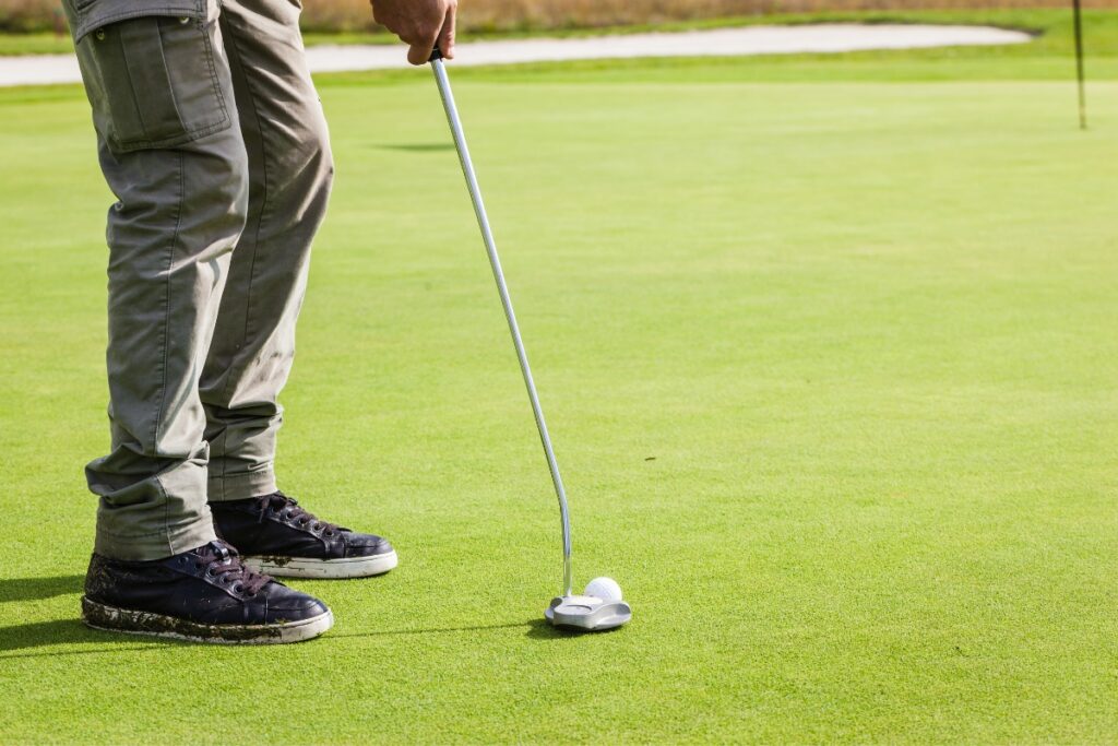 A man in pro golf apparel is putting a golf ball on the green.