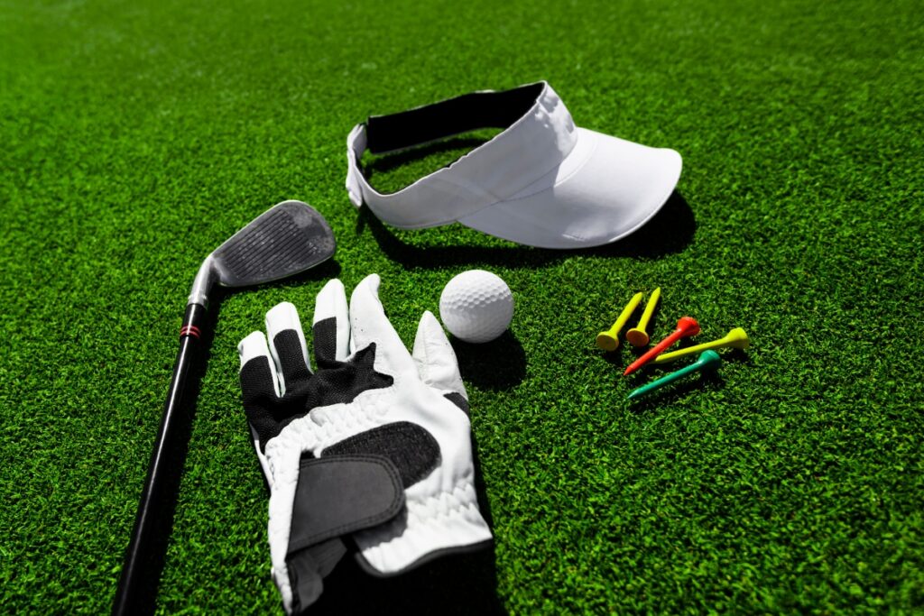 A pro golf club, glove, tee, and ball on green grass.