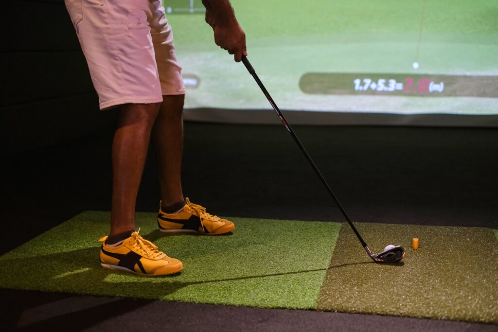 A man in pro golf apparel hitting a golf ball in a golf simulator.