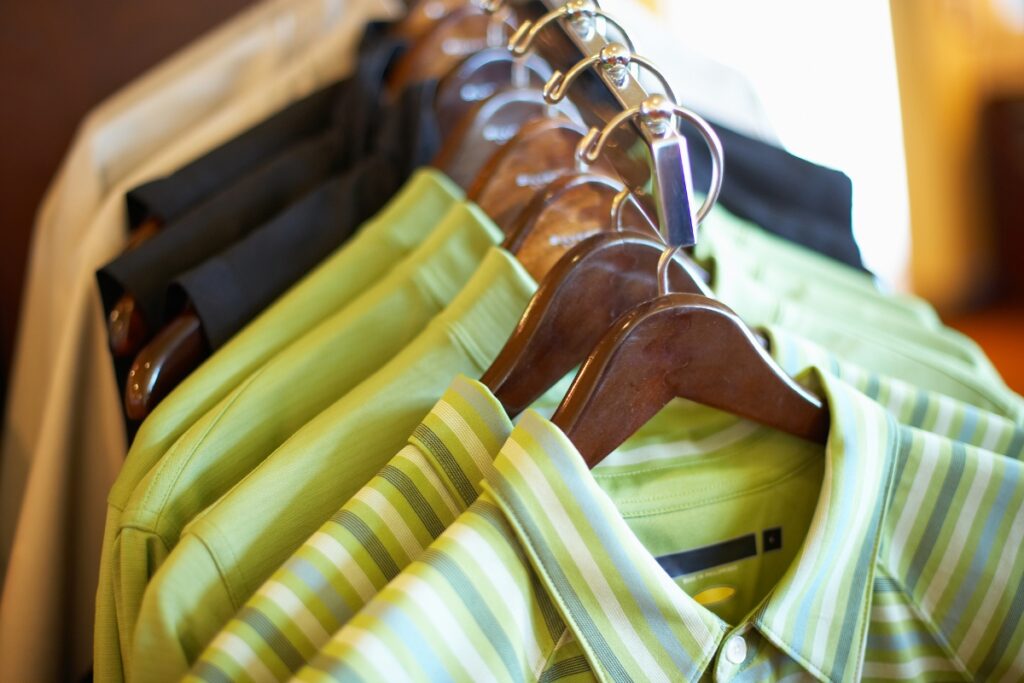 A row of striped and sustainable golf apparel shirts hanging on wooden hangers.