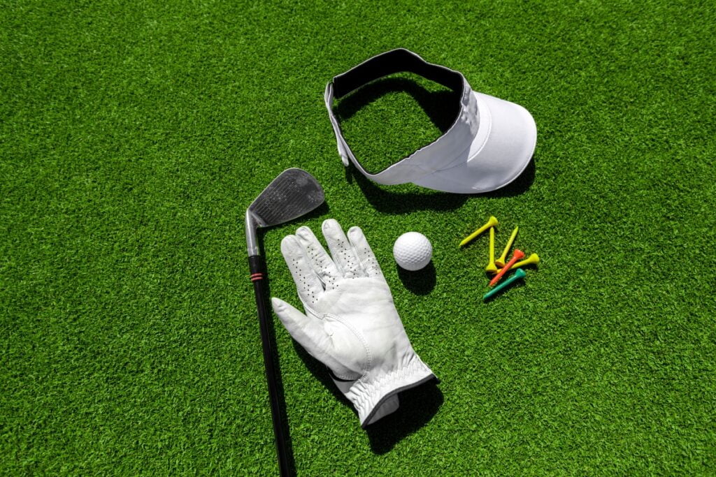 Golf equipment laid out on green turf, including a club, glove, ball, cap, and sustainable golf apparel.