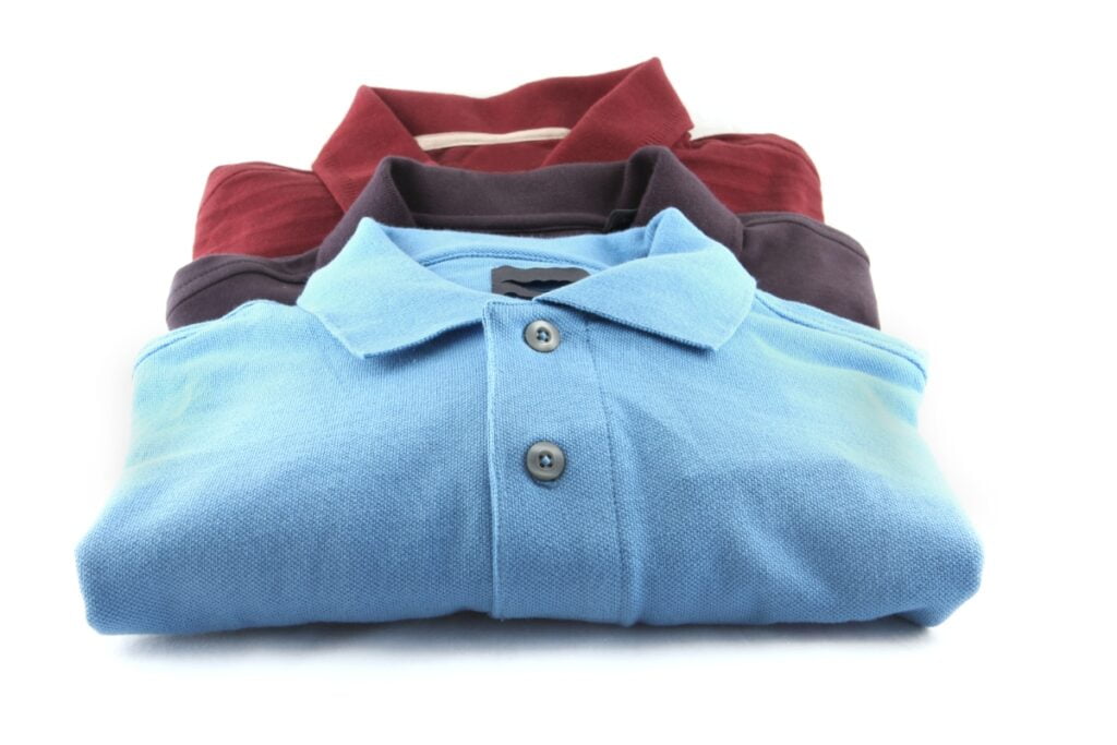 Stack of folded sustainable golf polo shirts in assorted colors.