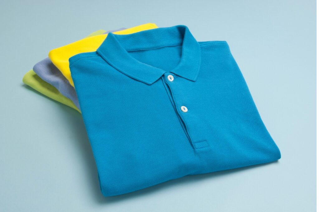 A stack of neatly folded polo shirts designed for golf in various colors including blue, yellow, and green, displayed on a light blue background.