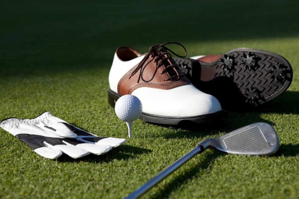 A pair of golf shoes, a golf ball, a club enhanced with golf technology, and a glove laid out on a grassy surface, symbolizing advanced golf equipment.