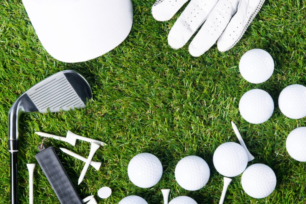 Golf accessories on grass, including a club, balls, tees, a glove, and a white hat.