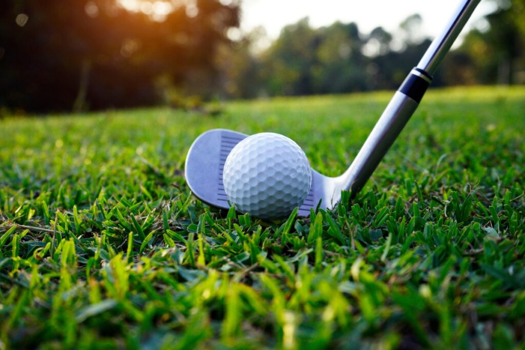 Golf accessories positioned for a swing on a grassy course at sunset.