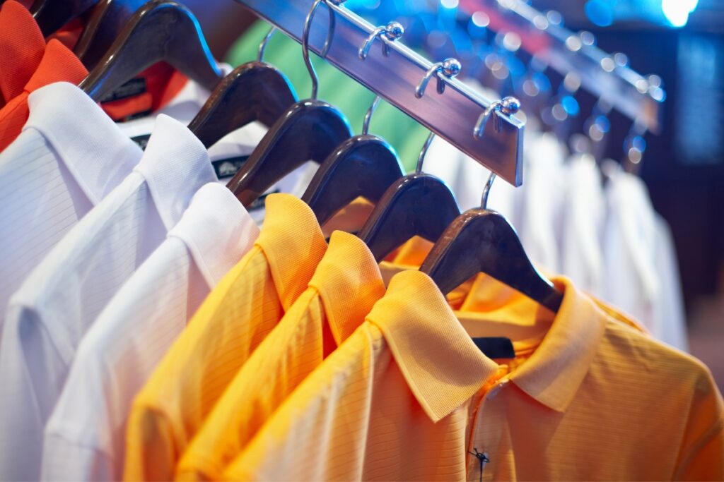 A row of colorful golf shirts hanging on metal hangers in a store, with focus on a yellow shirt.