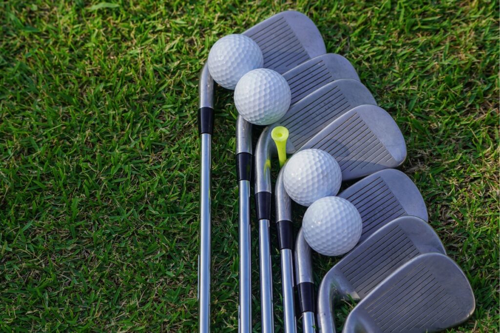 Golf accessories, including clubs and balls on grass, highlighting various irons and a tee, shot from a close angle.