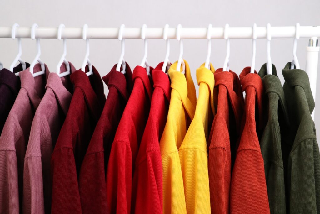 A line of colorful shirts from top golf apparel brands hanging on a white rack, featuring shades of red, yellow, and green.