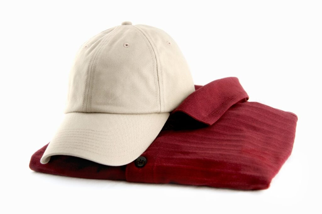 A beige baseball cap from a top golf apparel brand resting on top of a folded red polo shirt, both isolated on a white background.