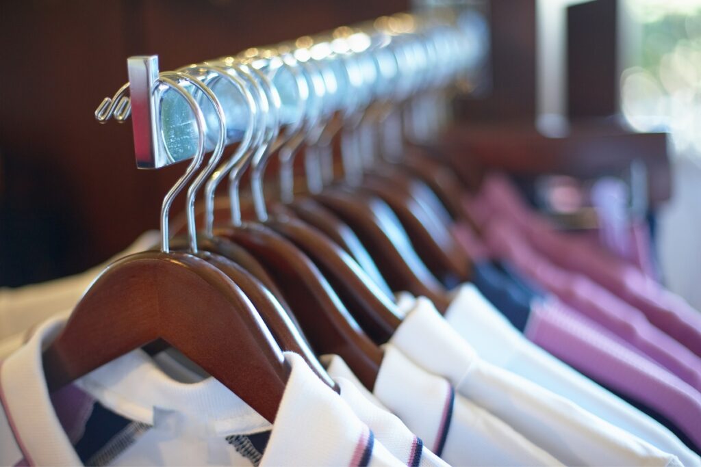 Row of wooden clothes hangers displaying various shirts from top golf apparel brands on a rack in a store.