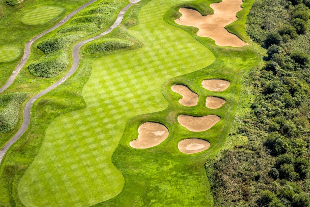 Aerial view of a golf course with green fairways, several sand bunkers, and adjacent rough vegetation, making it one of the premier golf travel destinations.