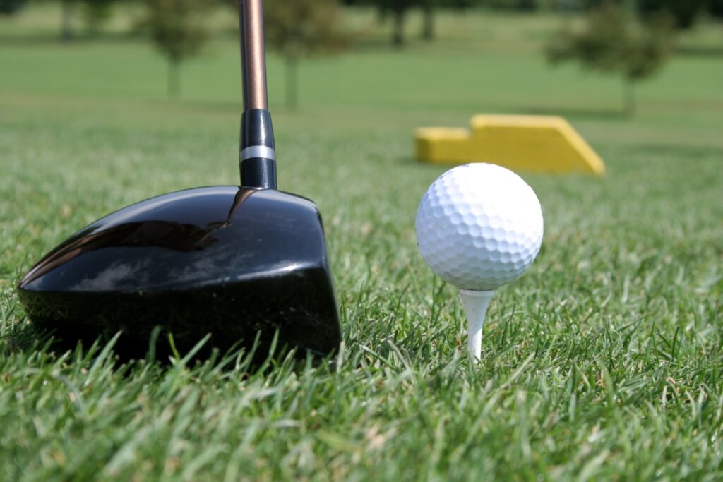 A golf club is positioned near a golf ball on a tee, ready for a swing, with the latest golf tech gadgets enhancing precision on the grassy course.