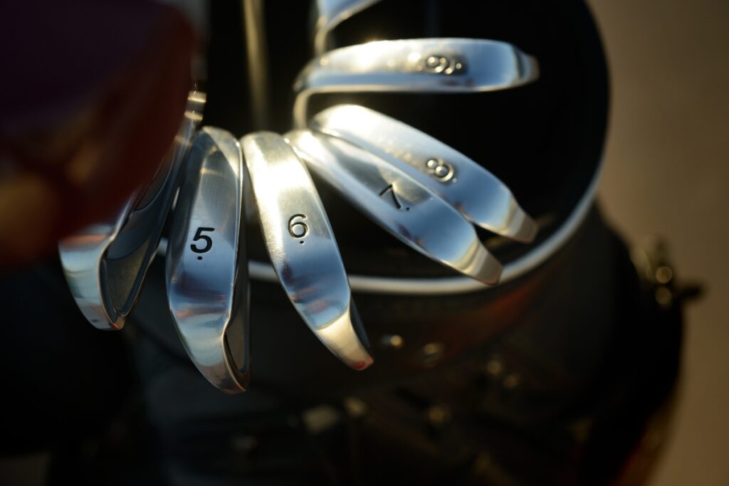 A close-up of a set of golf club irons arranged in a bag, with the numbers 5, 6, 7, 8, and 9 visible on the clubs’ heads. Subtle hints of cutting-edge golf tech gadgets enhance this premium setup.