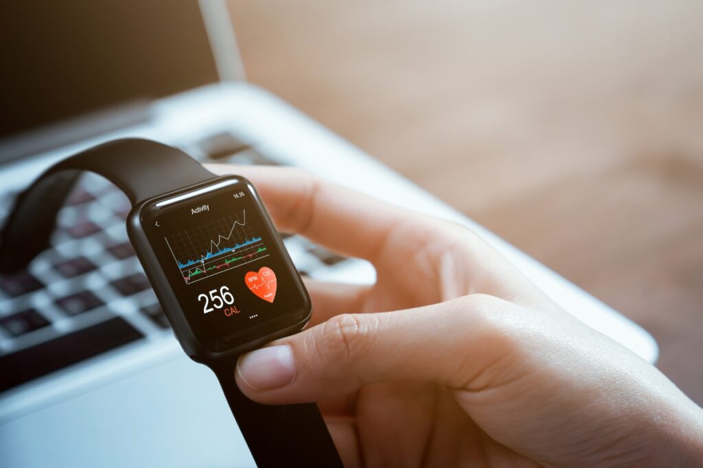 A hand holding a smartwatch displaying fitness data, including calories burned (256) and heart rate information, in front of a laptop keyboard. This sleek piece of golf tech seamlessly integrates with the latest gadgets to enhance your game and keep track of your performance metrics.