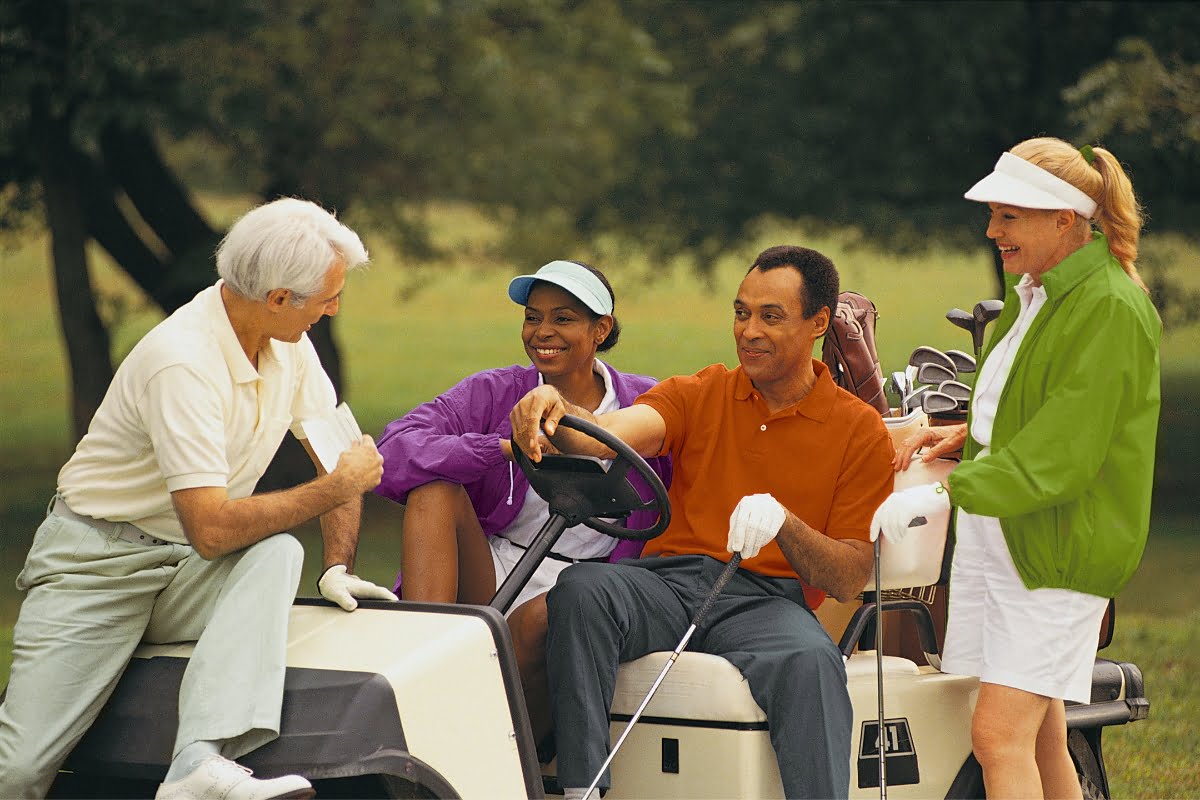 Four people are gathered around a golf cart in a grassy outdoor setting, holding golf clubs and dressed in casual golf attire. They appear to be enjoying a conversation before a game, blending the leisurely atmosphere with some subtle hints of golf business networking.