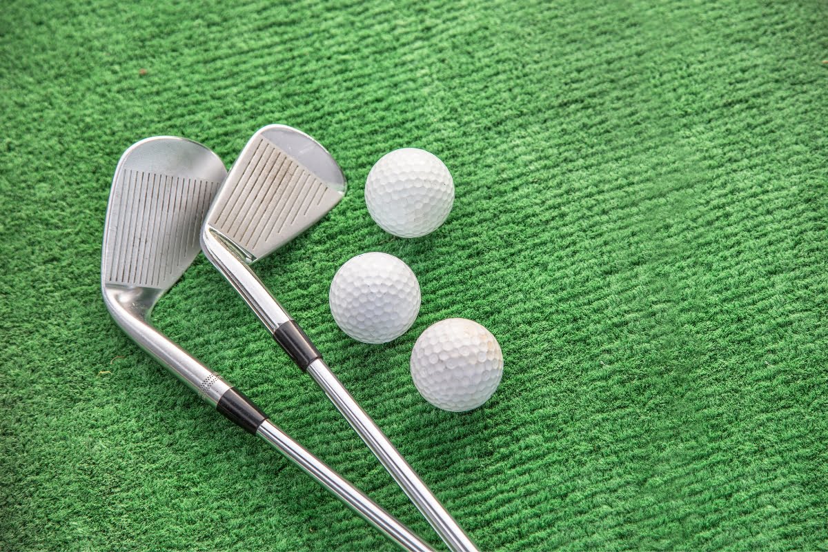 Two golf clubs and three golf balls on a green textured surface, ready for a perfect game of business networking on the course.