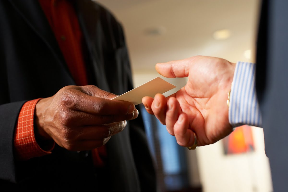 Two people exchanging a business card at a golf business networking event; one person extends the card while the other reaches to take it.