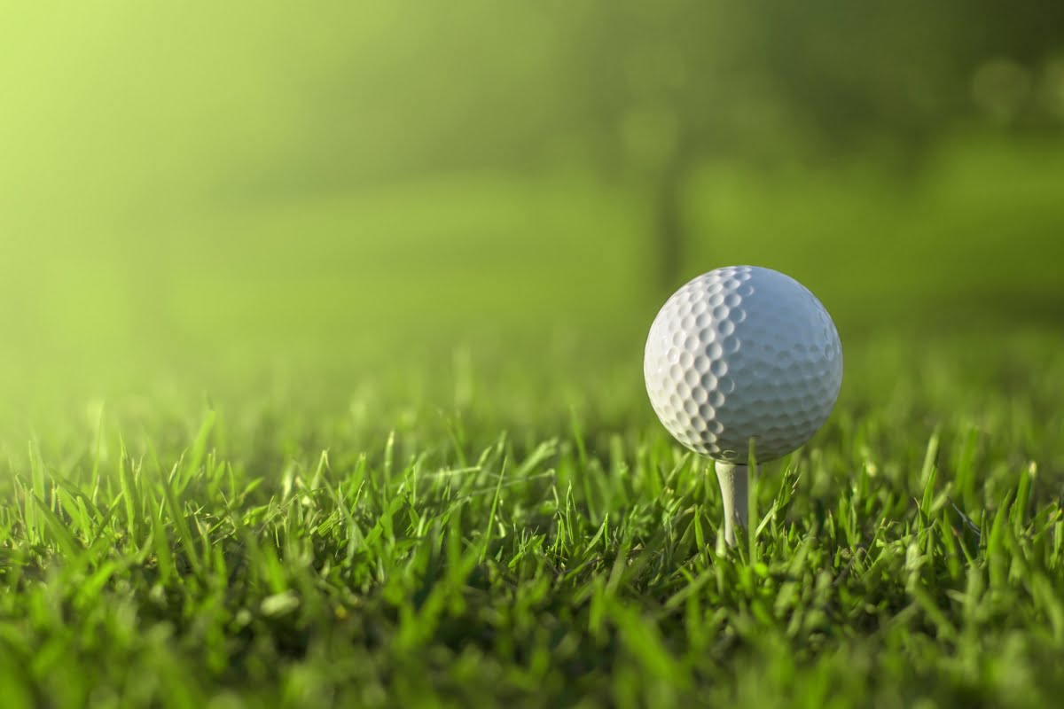 A golf ball is positioned on a tee in a lush, green field under bright sunlight, offering a moment of golf mindfulness amid the serene landscape.