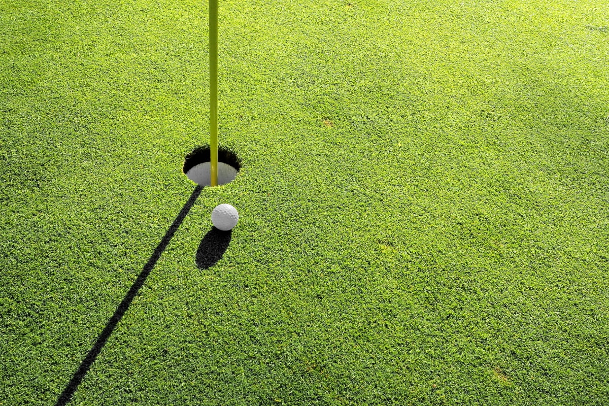 A golf ball sits just outside the rim of a hole on a bright green putting green, with a yellow flagstick casting a shadow—an ideal scene for practicing golf mindfulness.