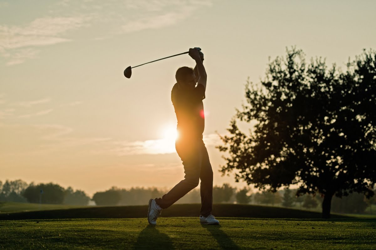 A silhouette of a golfer taking a swing on a golf course at sunrise, embracing golf mindfulness with trees in the background.