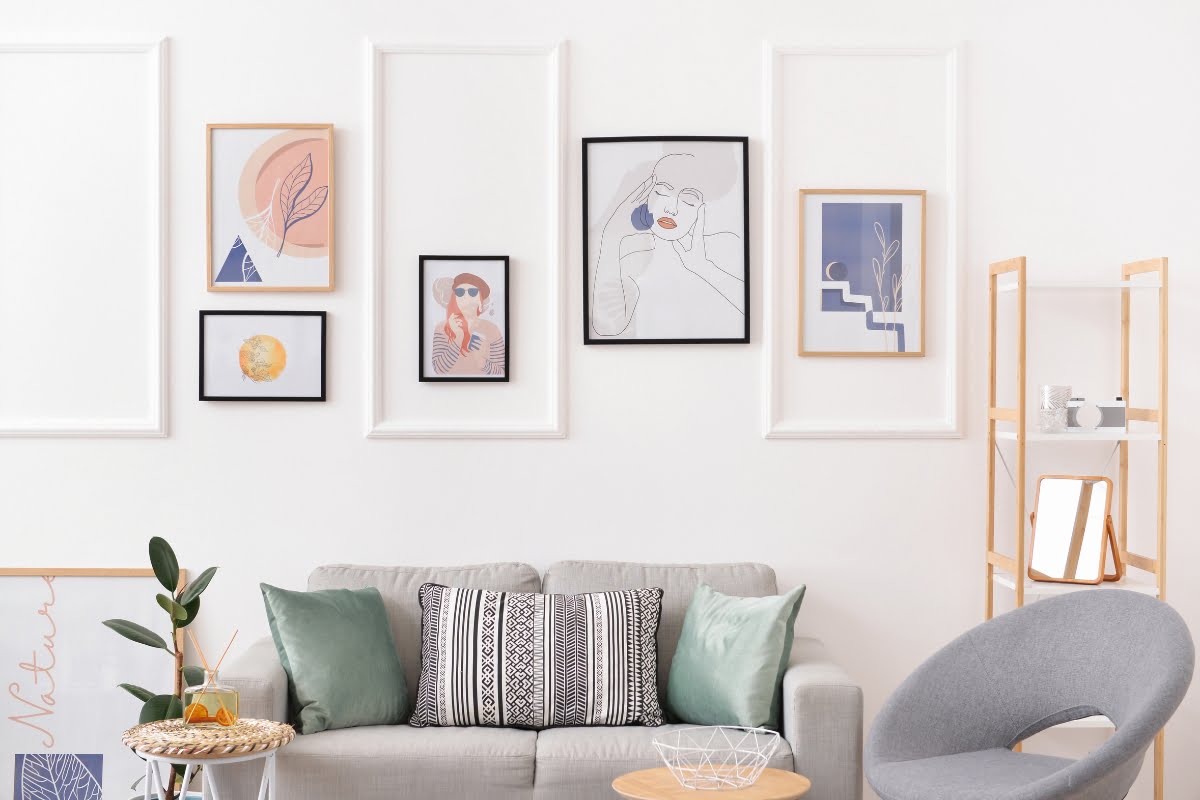 A modern living room features a gray sofa with patterned and solid pillows, a round wooden table, a gray chair, and framed artworks on a white wall. A wooden screen stands on the right, complemented by subtle golf home decor accents for an extra touch of sophistication.