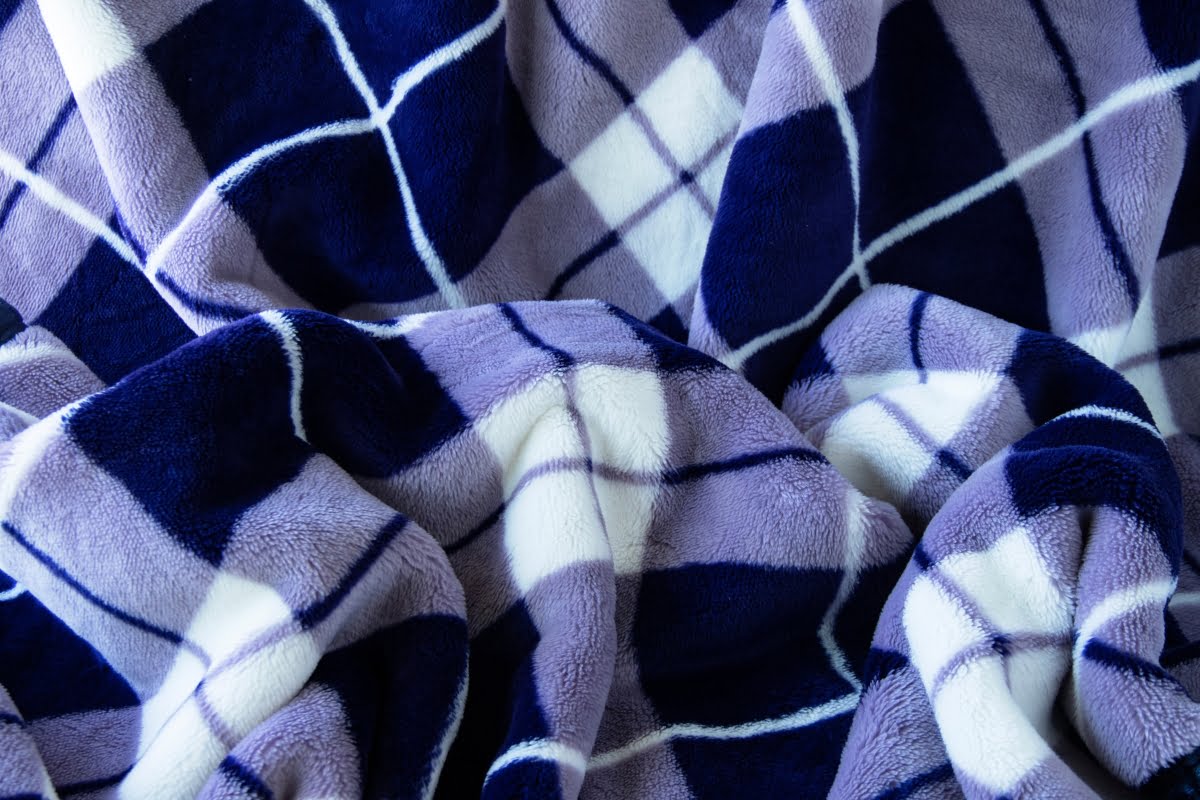 A close-up of a soft, plaid blanket in shades of blue, white, and light purple. The fabric is crumpled, showcasing the various colors and patterns—a perfect addition to cozy golf home decor.