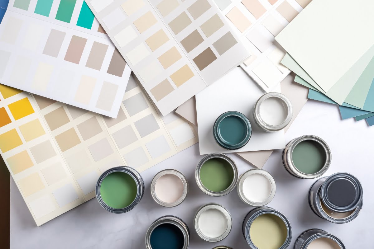 Various paint color samples, swatches, and open cans of paint in shades of green, blue, and neutral tones are spread out on a surface—perfect for creating a serene golf-inspired home decor.