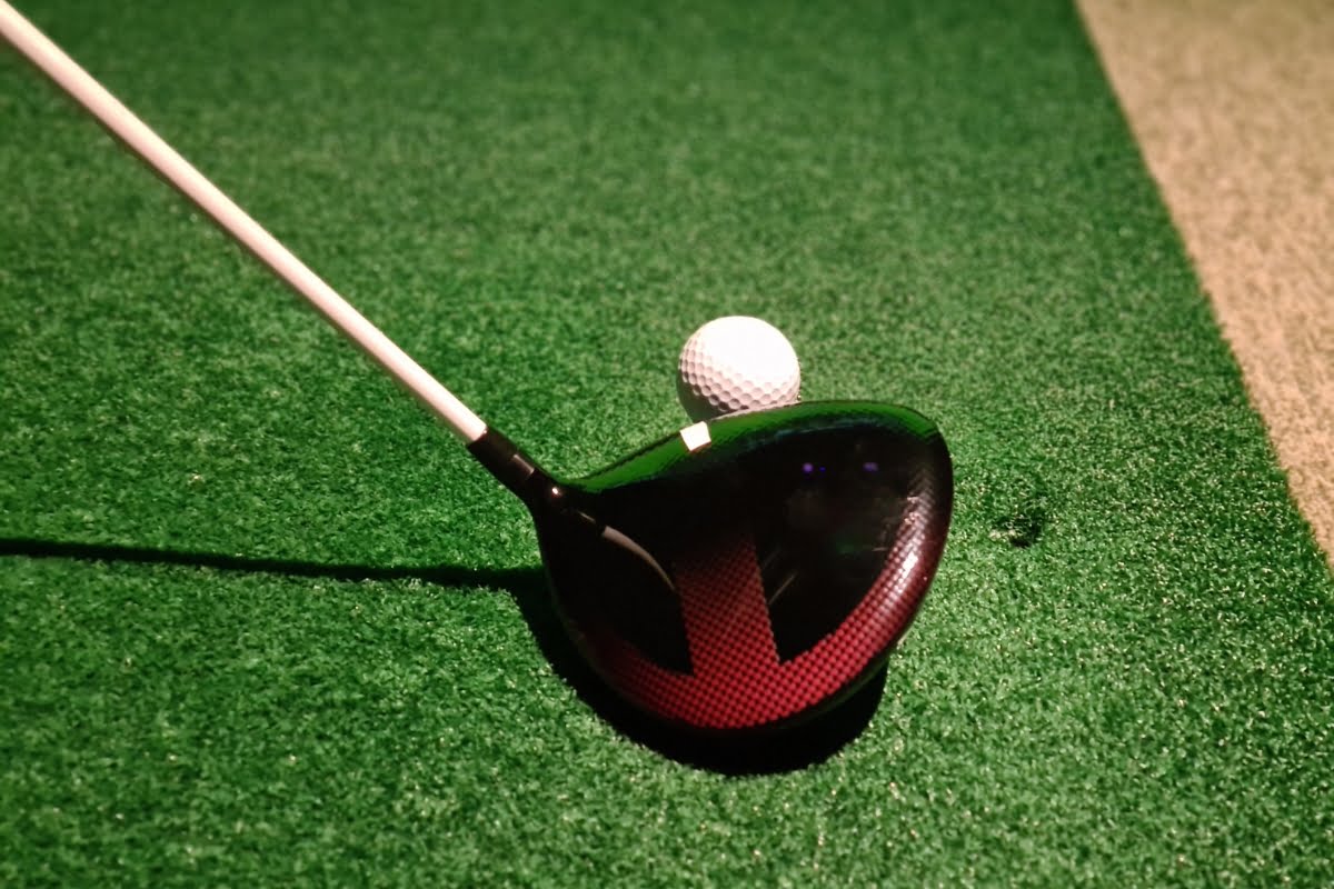 A golf club is positioned behind a golf ball on artificial green turf, ready for a shot, creating an elegant touch for golf home decor.