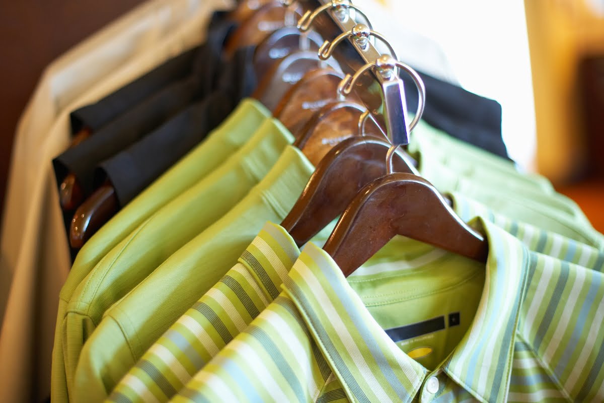 A row of green and black collared shirts for golfing in cold weather, displayed on wooden hangers on a clothing rack.