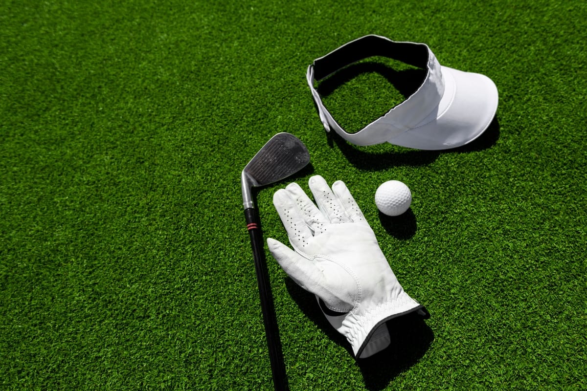 A golf club, white glove, golf ball, and visor lie on the green grass, embodying the essence of peak golf performance.