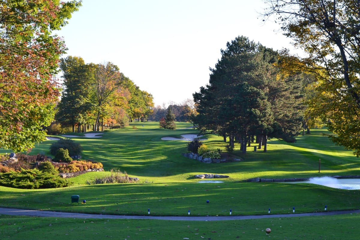 A sustainable golf course featuring green fairways, trees lining the sides, sand bunkers, and a blue sky offers an eco-friendly escape into nature.