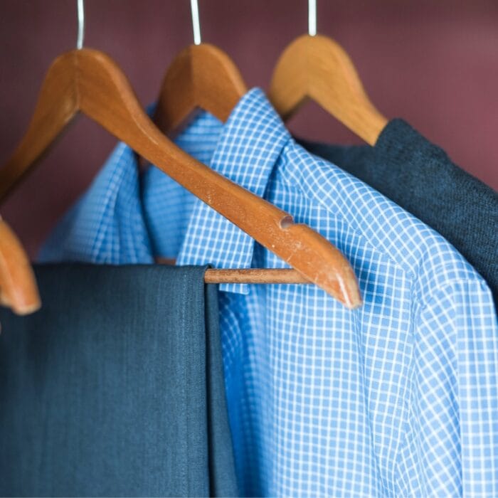 Wooden hangers hold a blue checkered shirt, a dark suit jacket, and matching trousers in a closet, perfectly complementing professional golf attire.