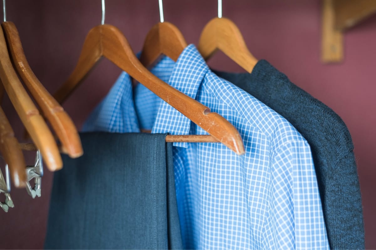 Wooden hangers hold a blue checkered shirt, a dark suit jacket, and matching trousers in a closet, perfectly complementing professional golf attire.