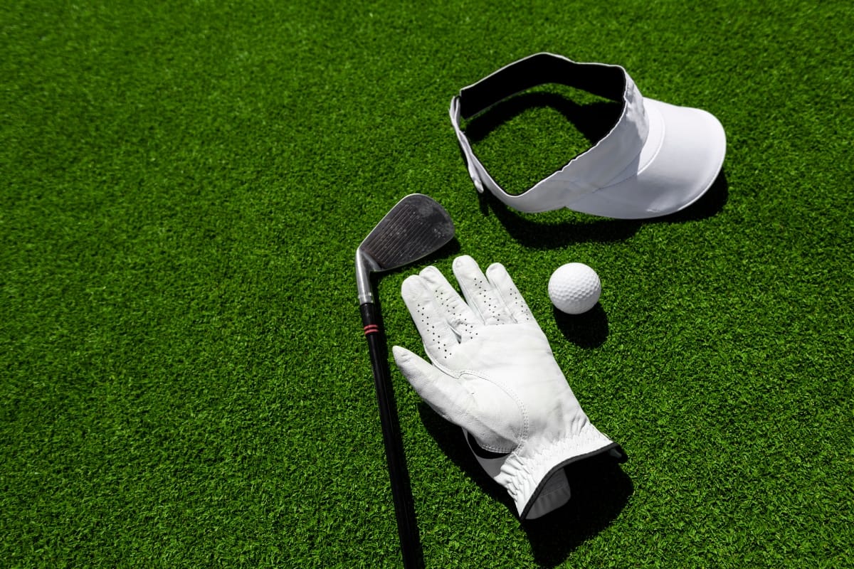 Golf club, white visor, glove, and ball on green turf.