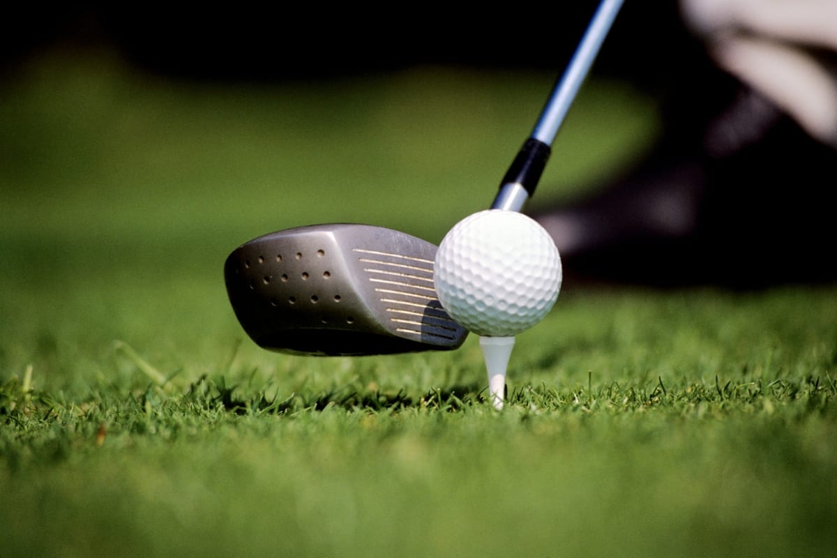 A golf club is poised to strike a golf ball resting on a white tee on lush green grass—perfect attire for this moment would include the best golf shorts for comfort and style.