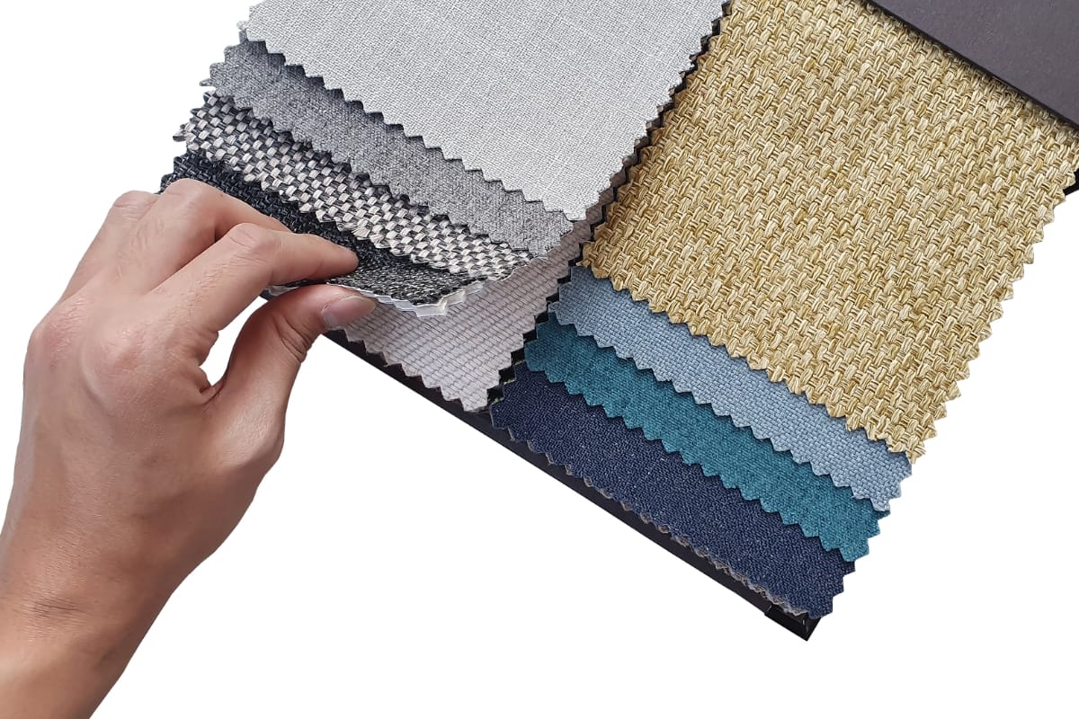 A hand holding a sample book of fabric swatches in various colors and textures, perfect for selecting the material for the best golf shorts.
